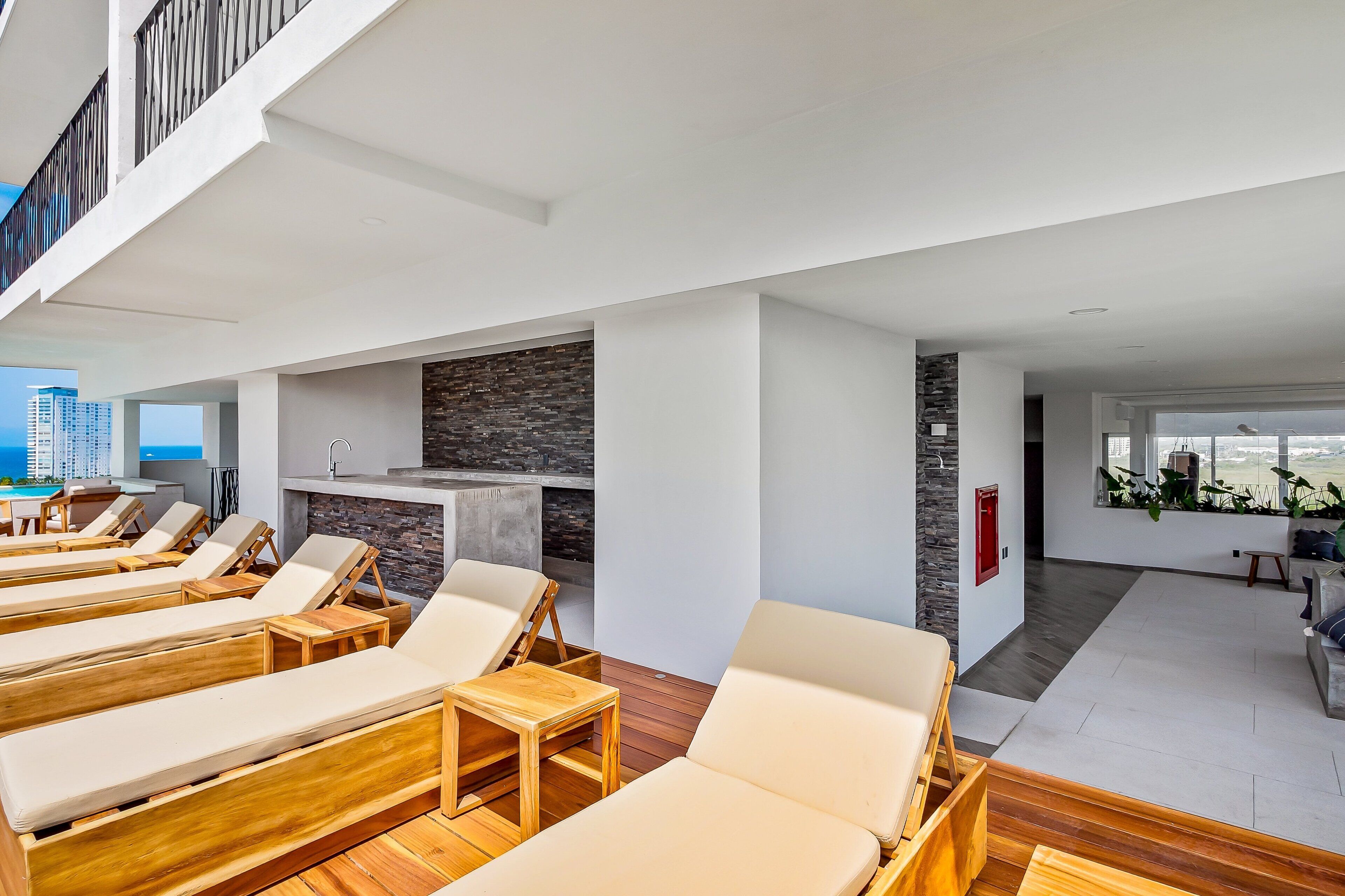 A modern lounge area with sun loungers, a stone wall, and a view of the city.