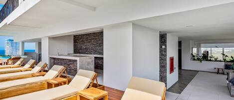 A modern lounge area with sun loungers, a stone wall, and a view of the city.