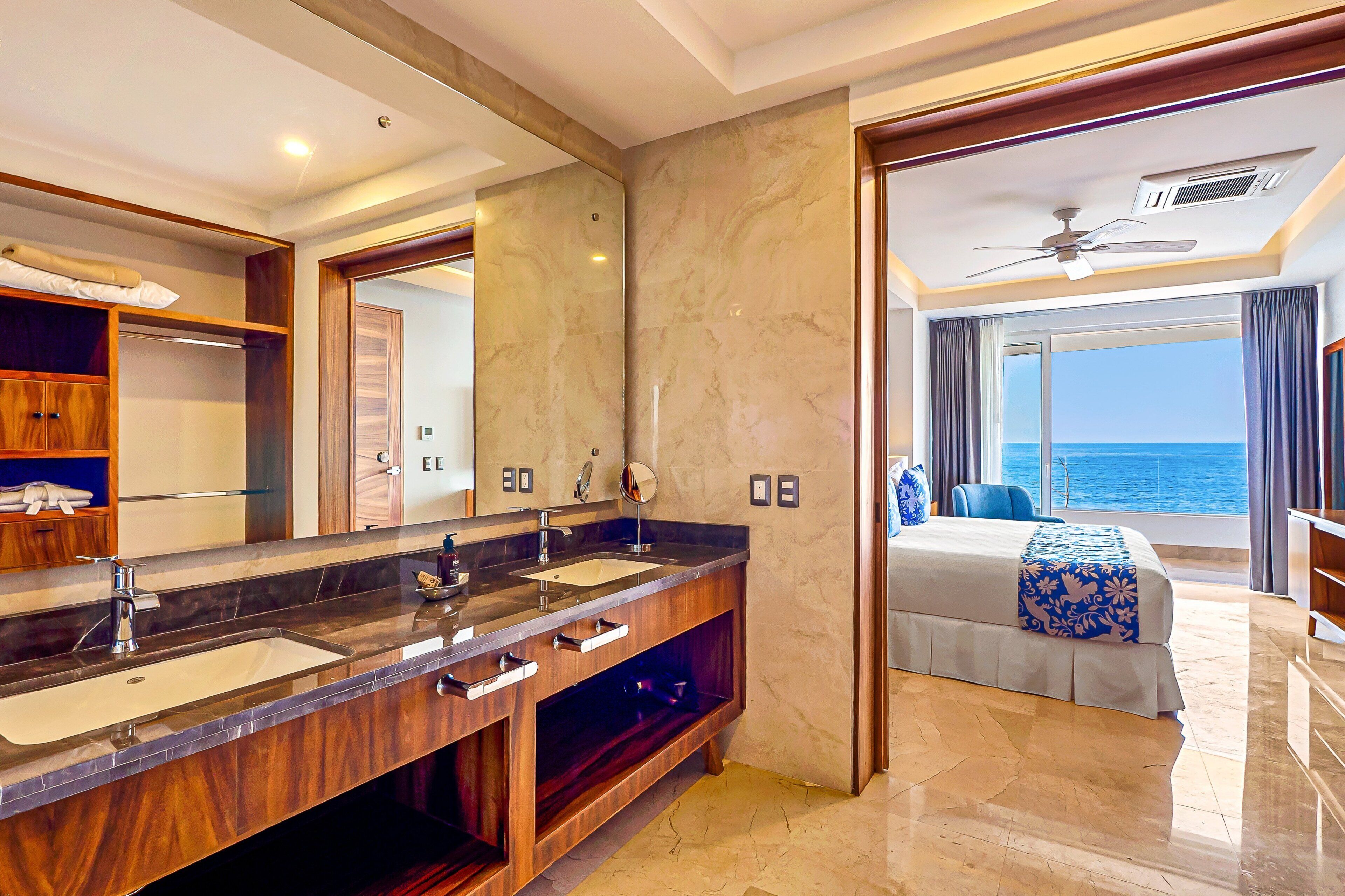 Een moderne hotelkamer met een ruime badkamermeubel, een bed met uitzicht op zee en een plafondventilator.