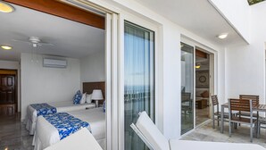 A hotel room with a bed, a sofa, a glass door leading to a balcony, and a dining area with chairs and a table. - Elegant Bayview Suite With Terrace Access, Full Kitchen, Pool, hot tub & gym (Puerto Vallarta)