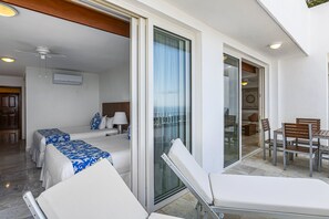 Ein Hotelzimmer mit einem Bett, einem Sofa, einer Glastür, die auf einen Balkon führt, und einem Essbereich mit Stühlen und einem Tisch.