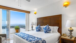 A hotel room with a large bed, two bedside lamps, a wooden headboard, a nightstand, a telephone, and a balcony with a potted plant. - Elegant Bayview Suite With Terrace Access, Full Kitchen, Pool, hot tub & gym (Puerto Vallarta)
