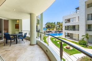 Un balcón con mesa y sillas, una piscina y un jardín bien cuidado.