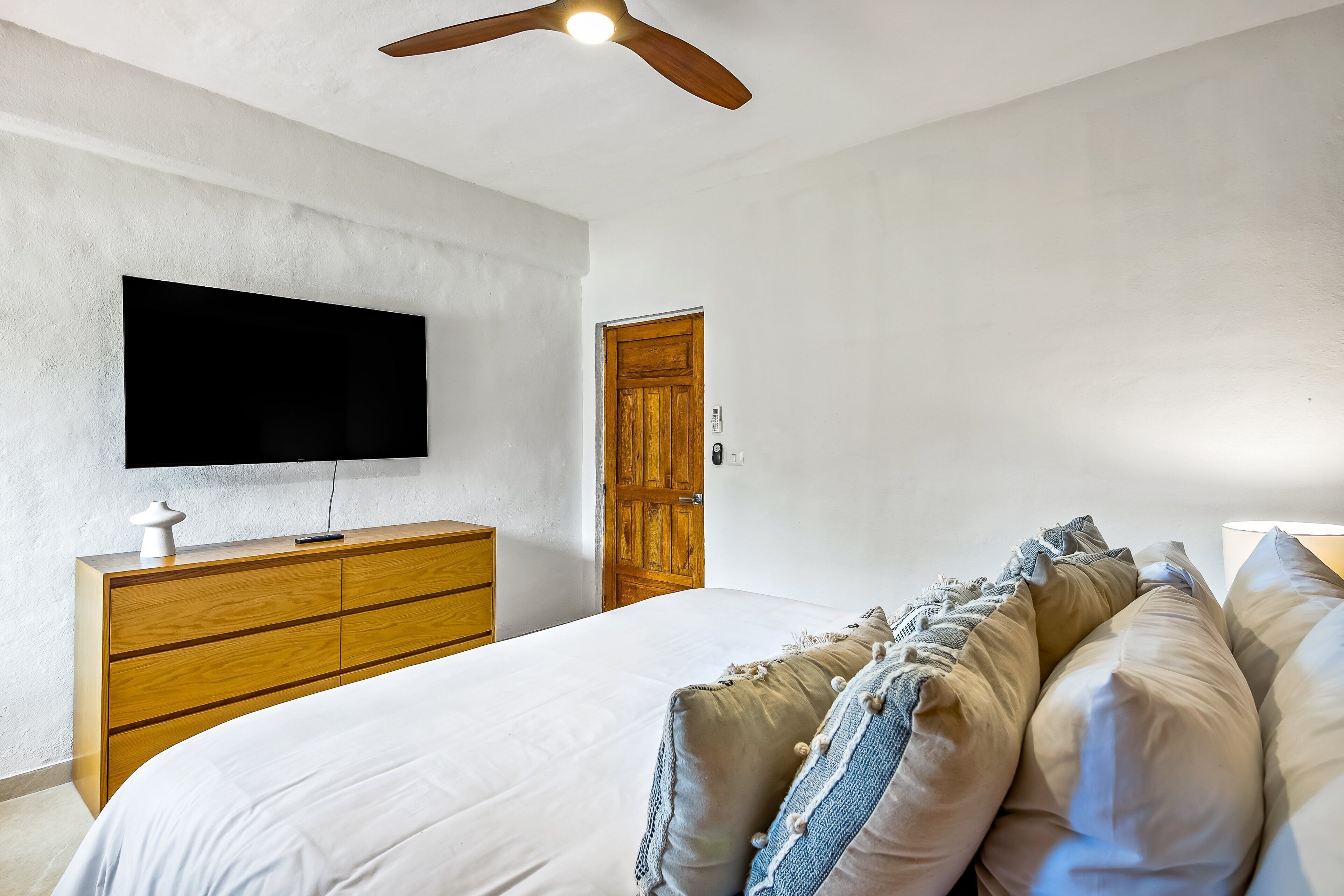 A bedroom with a bed, wooden dresser, television, and a ceiling fan.