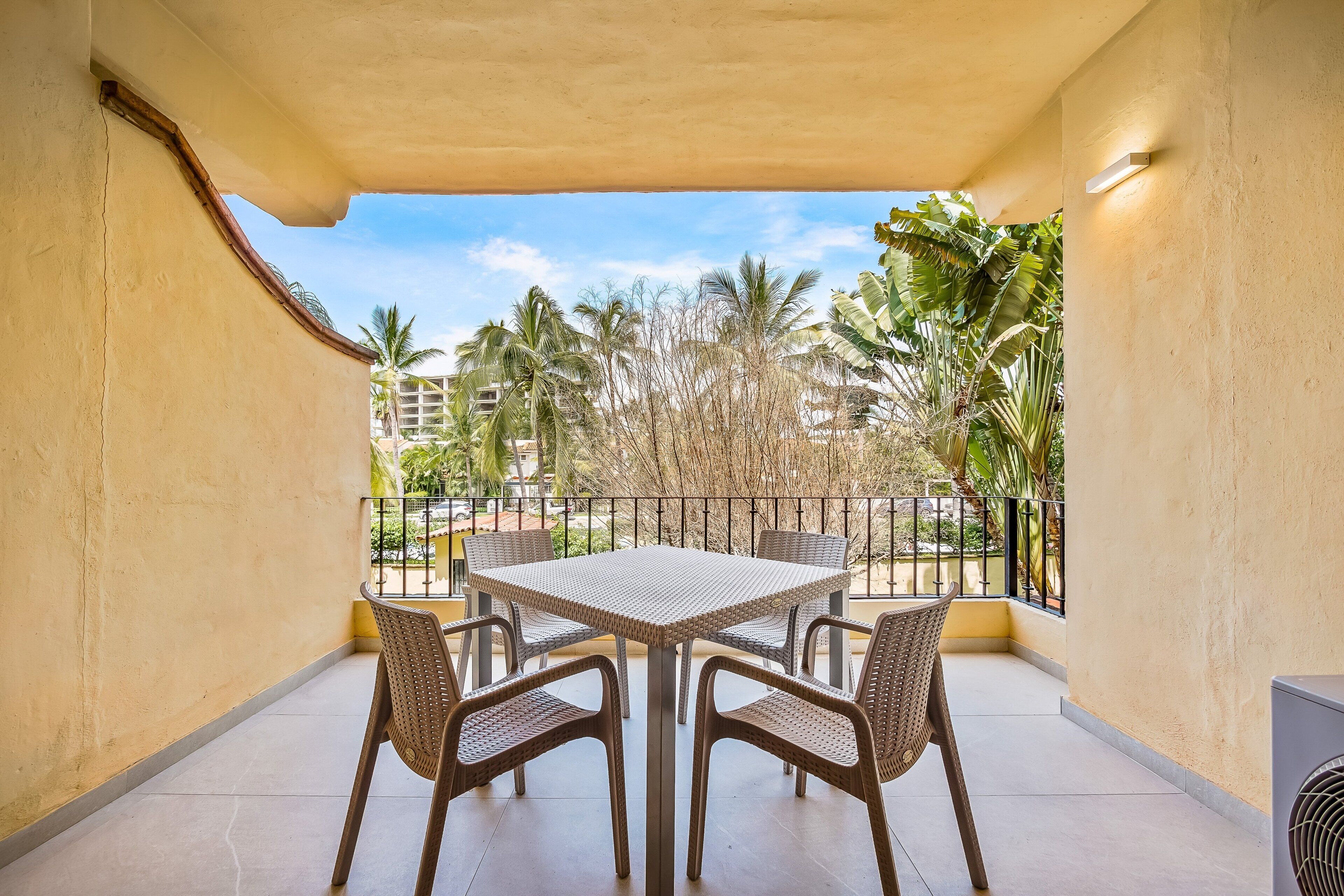 A balcony with a table and chairs, a view of palm trees, and a building in the background.