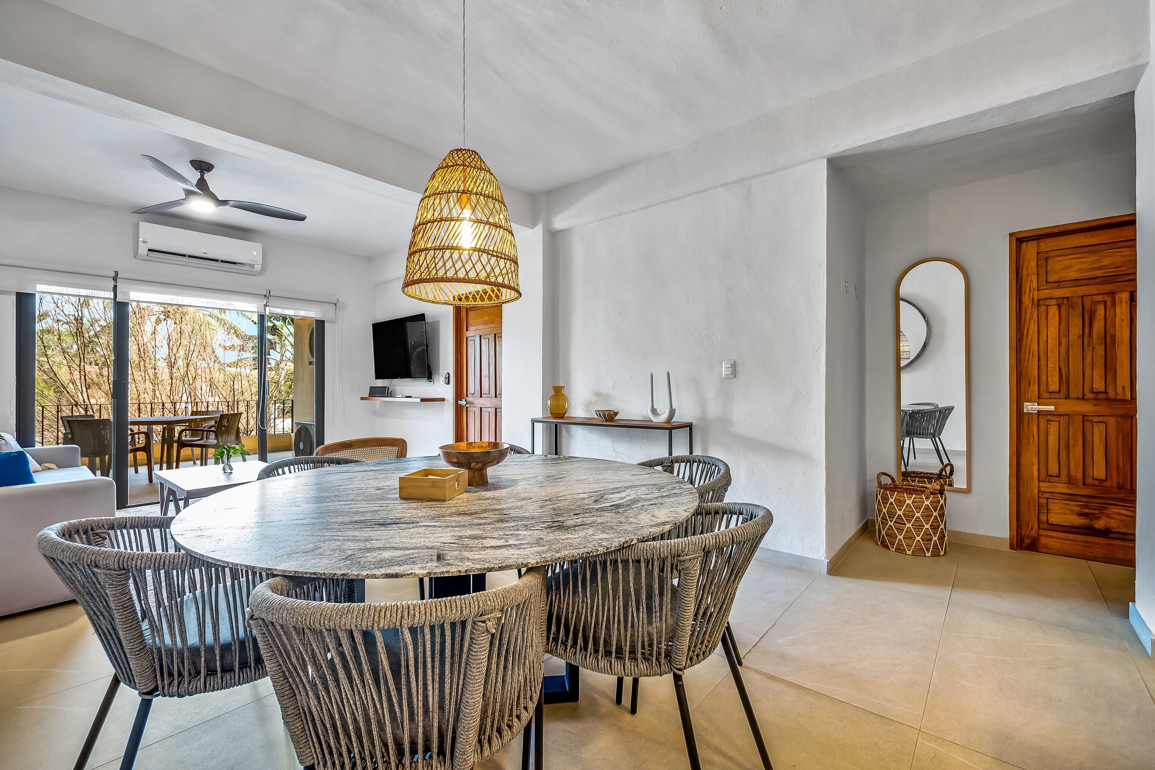A dining area with a round table, wicker chairs, a ceiling fan, and a hanging light fixture.