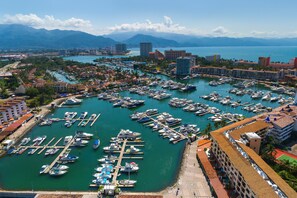 Una marina con numerosos barcos amarrados, rodeada de edificios y montañas al fondo.