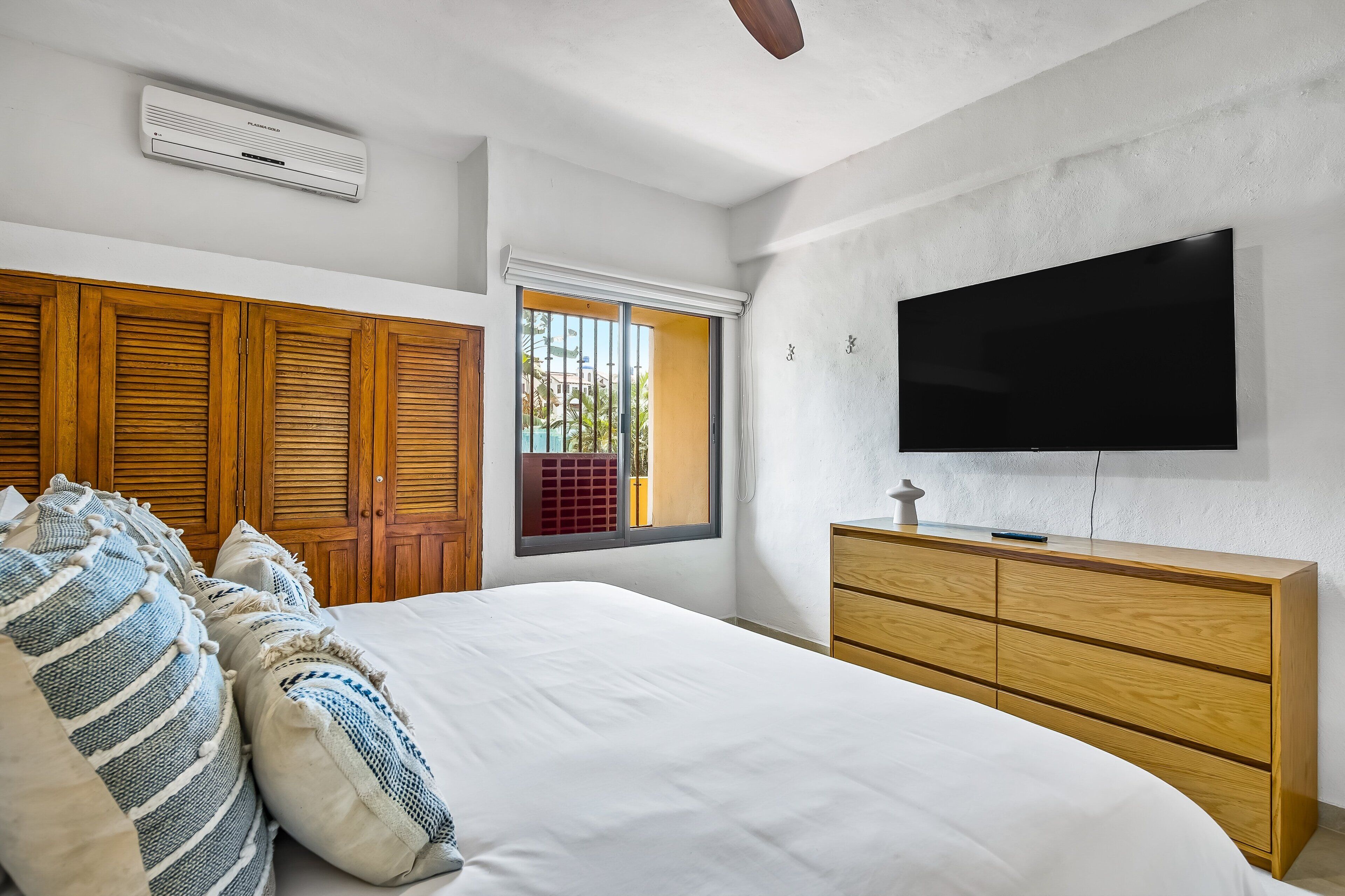A bedroom with a bed, wooden wardrobe, a television, and a window.