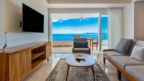 Ett modernt vardagsrum med en platt-TV, en TV-möbel i trä, en soffa, ett soffbord och en balkong med utsikt över havet.
