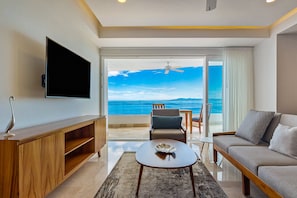 A modern living room with a flat-screen TV, a wooden entertainment unit, a sofa, a coffee table, and a balcony with a view of the sea. - Stylish Waterfront Condo With Amazing Pool, hot tub & Balcony (Puerto Vallarta)