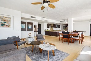 En moderne stue med spiseplads, en ventilator i loftet og et køkken i baggrunden.