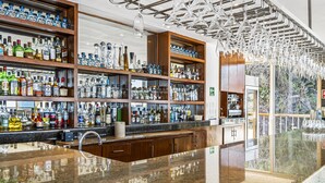 Baarissa on hyllykkö täynnä alkoholijuomapulloja, kiillotettu graniittitaso ja moderni kattokruunu.
