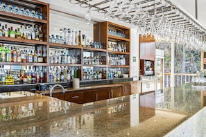 A bar with shelves of liquor bottles, a polished granite countertop, and a modern chandelier. - Stunning Oceanview Suite With Cliffside Infinity Pool, Terrace & Gourmet Kitchen (Puerto Vallarta)