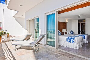 Un balcon avec des chaises longues et un lit recouvert d’une courtepointe bleue et blanche.