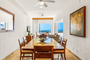 Un coin repas comprenant une grande table, des chaises, un ventilateur de plafond et un tableau accroché au mur.