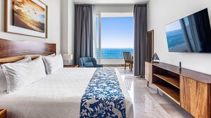 A hotel room with a large bed, a TV, a view of the ocean, and a balcony with a chair. - Luxury Bayfront Condo With Amazing Views, Pool & spa (Puerto Vallarta)