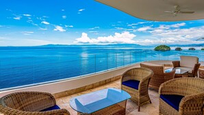 A balcony with wicker furniture, a glass table, and a view of the ocean. - Luxury Bayfront Condo With Amazing Views, Pool & spa (Puerto Vallarta)