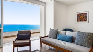 A modern living room with a sofa and armchair, a large window with a view of the ocean, and a framed artwork on the wall. - Luxury Bayfront Condo With Amazing Views, Pool & spa (Puerto Vallarta)