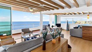 A spacious living area with a view of the sea, wooden ceiling beams, and a modern kitchen area. - Stylish Coastal Condo With Pool, Private Balcony & Stunning Ocean Views (Puerto Vallarta)