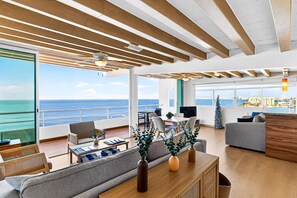 Amplia sala de estar con vista al mar, vigas de madera en el techo y una moderna zona de cocina.