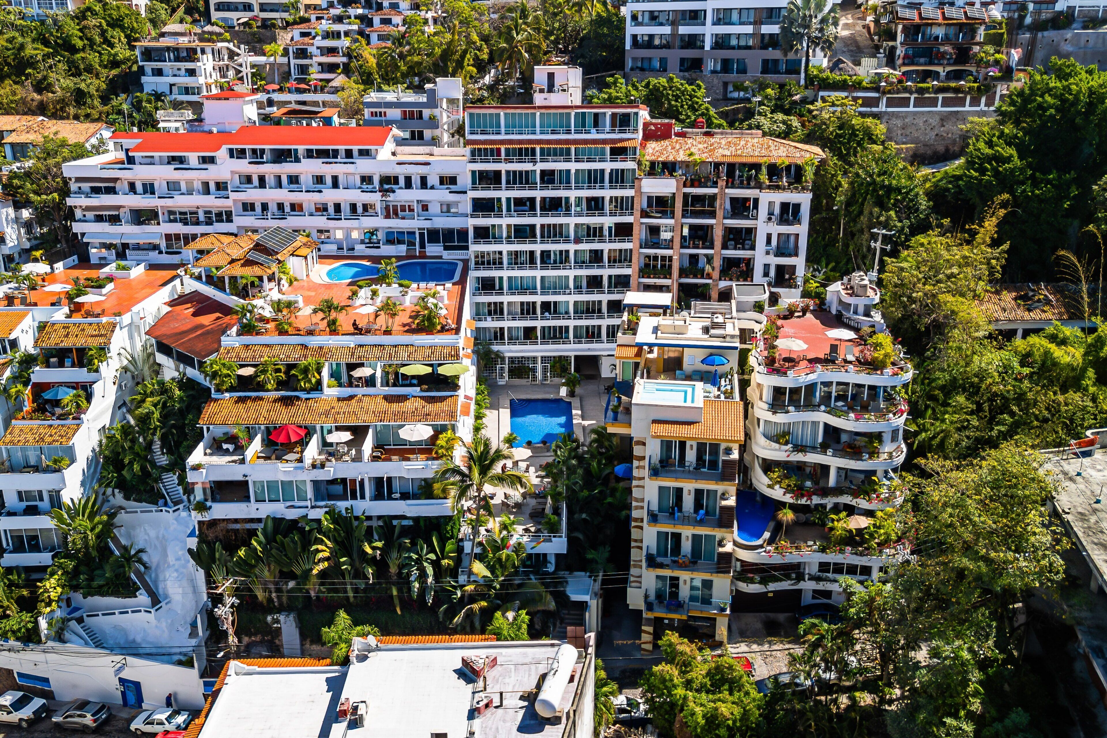 Un hotel de varios pisos con balcones, piscina y abundante vegetación.