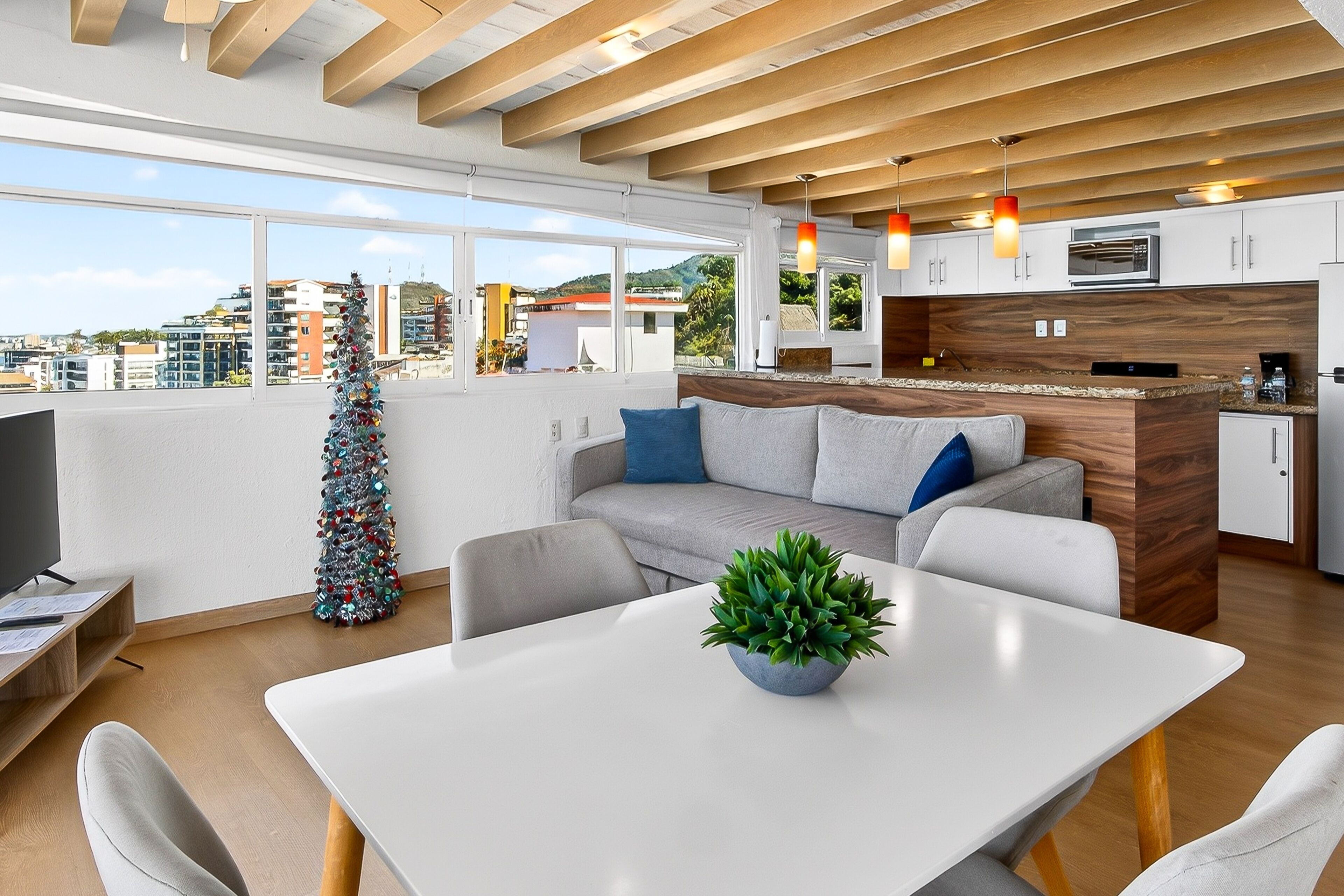 A modern living space with a dining area, kitchen, and large windows offering a city view.
