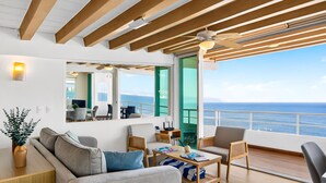 Una sala de estar moderna con un sofá, una mesa de centro y sillas, un comedor con mesa y sillas, y un ventanal con vistas al mar.