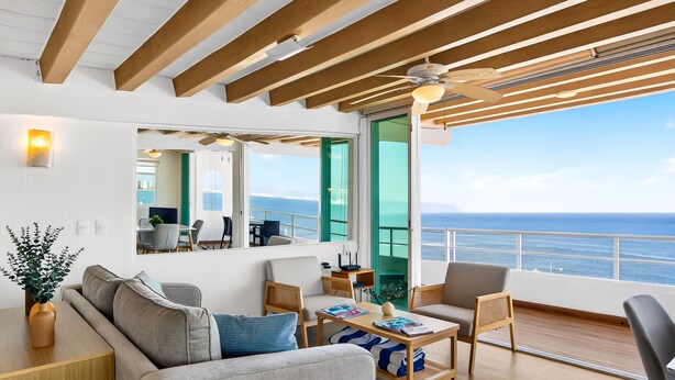 A modern living room with a sofa, coffee table, and chairs, a dining area with a table and chairs, and a large window with a view of the sea. - Stylish Coastal Condo With Pool, Private Balcony & Stunning Ocean Views (Puerto Vallarta)