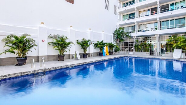 Una piscina con macetas y un edificio con balcones.