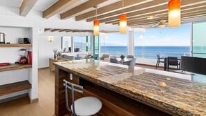 A modern kitchen with a granite countertop, wooden beams, and pendant lights. - Stylish Coastal Condo With Pool, Private Balcony & Stunning Ocean Views (Puerto Vallarta)