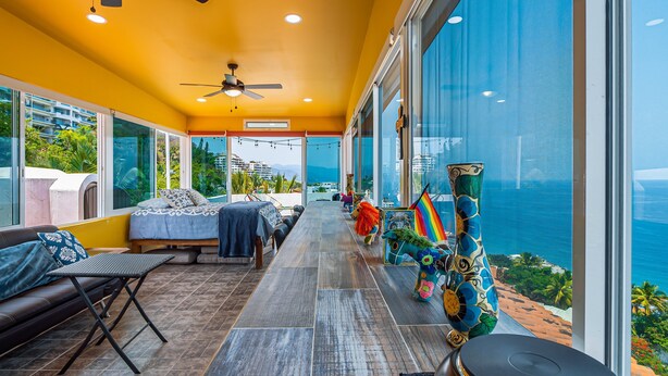 A balcony with a view of the ocean, a sofa, a dining table, and a ceiling fan. - Gardenias Studio Studio in Puerto Vallarta With Panoramic Views (Puerto Vallarta)