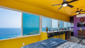 A room with a large window, a bed, a ceiling fan, and a bar area. - Gardenias Studio Studio in Puerto Vallarta With Panoramic Views (Puerto Vallarta)