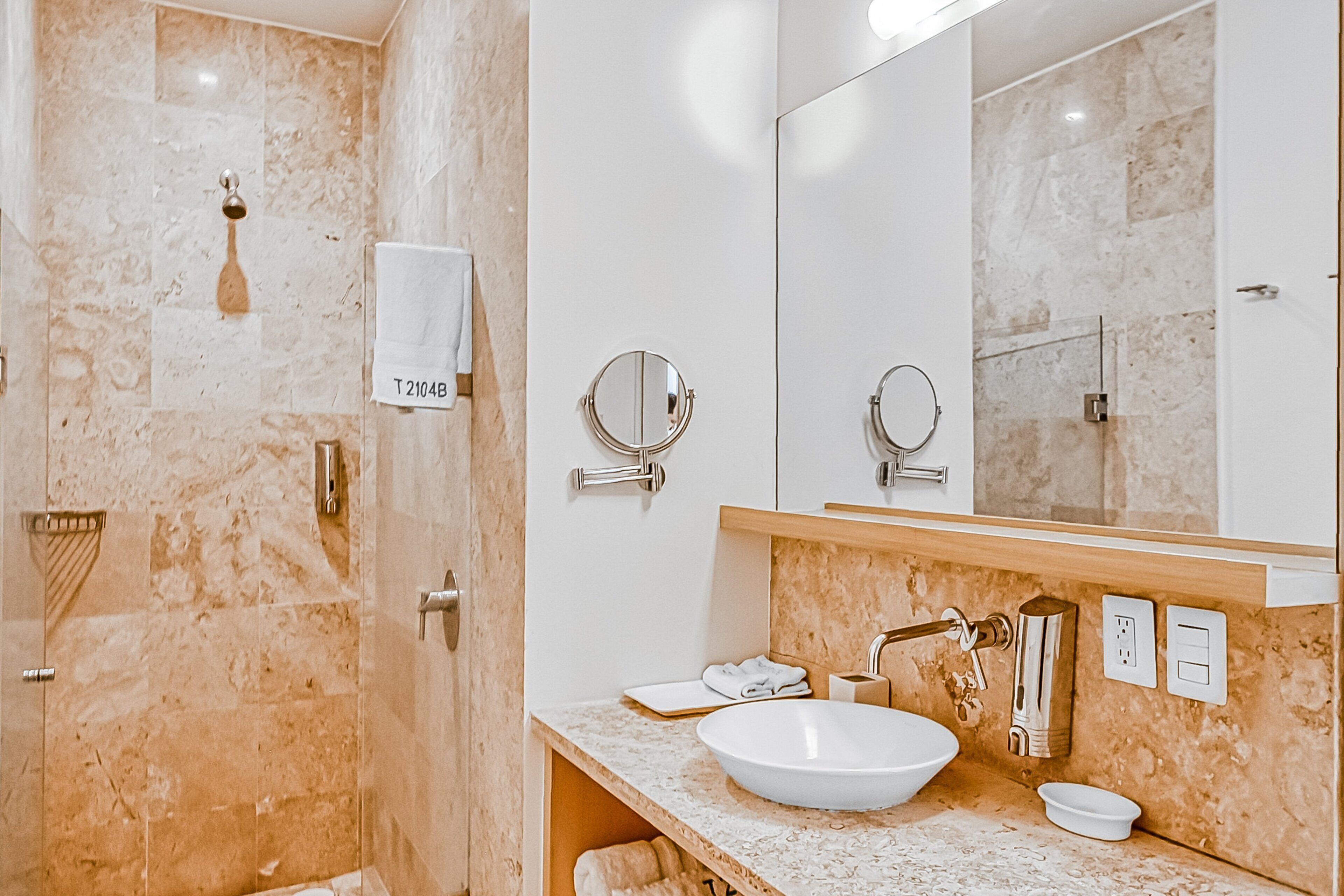 Een badkamer met een marmeren douche, een wastafel met een grote spiegel en een handdoekrek.