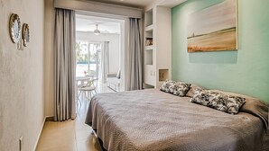 Ein Schlafzimmer mit Bett, Vorhängen, Deckenventilator, einem Gemälde und Blick ins Freie.