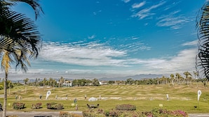 Ein Golfplatz mit blauem Himmel, Palmen und Bergen im Hintergrund.