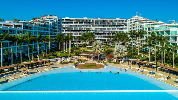 Een hotel met een groot zwembad, palmbomen en een modern architectonisch ontwerp.