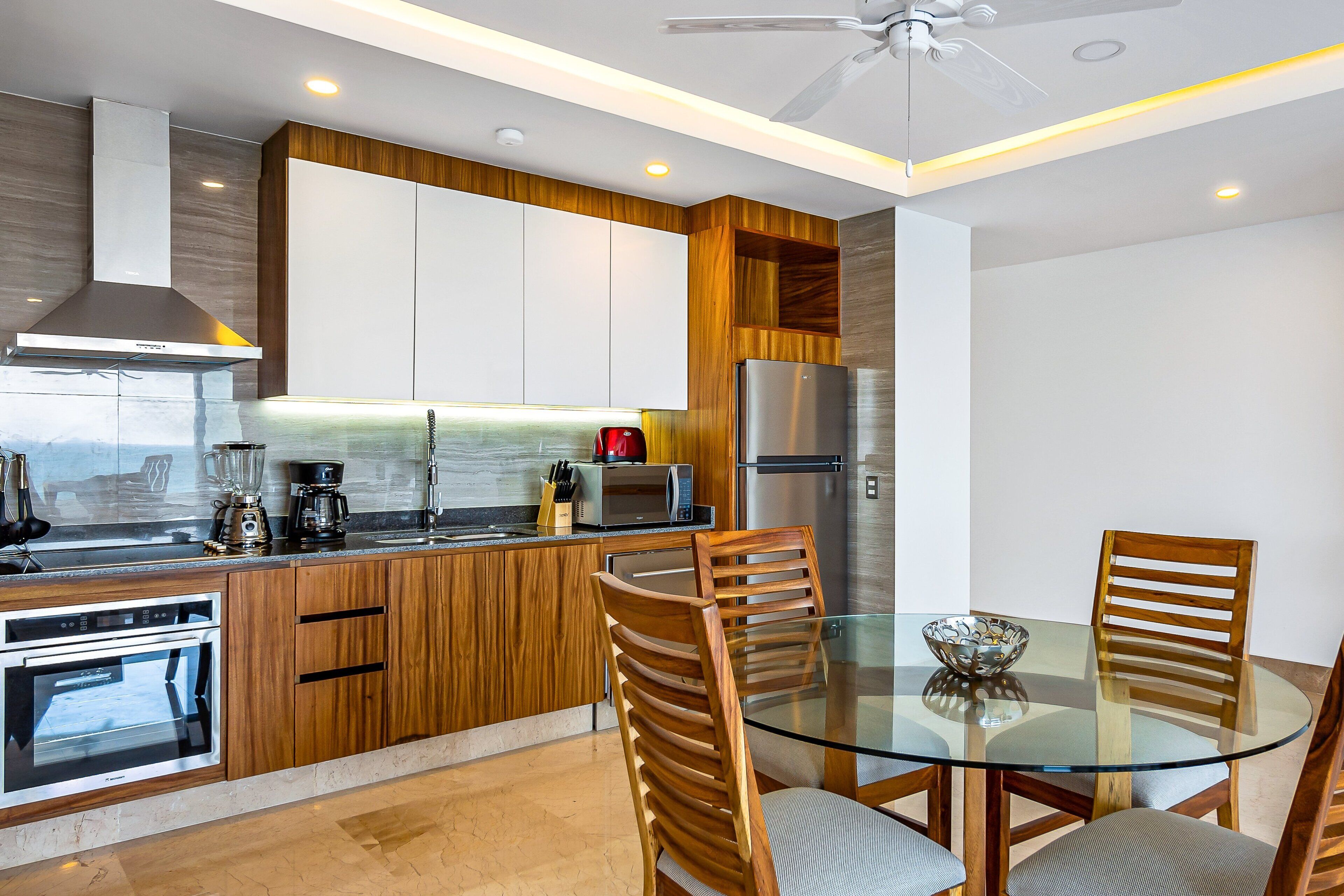 A modern kitchen with wooden cabinets, stainless steel appliances, and a glass dining table.