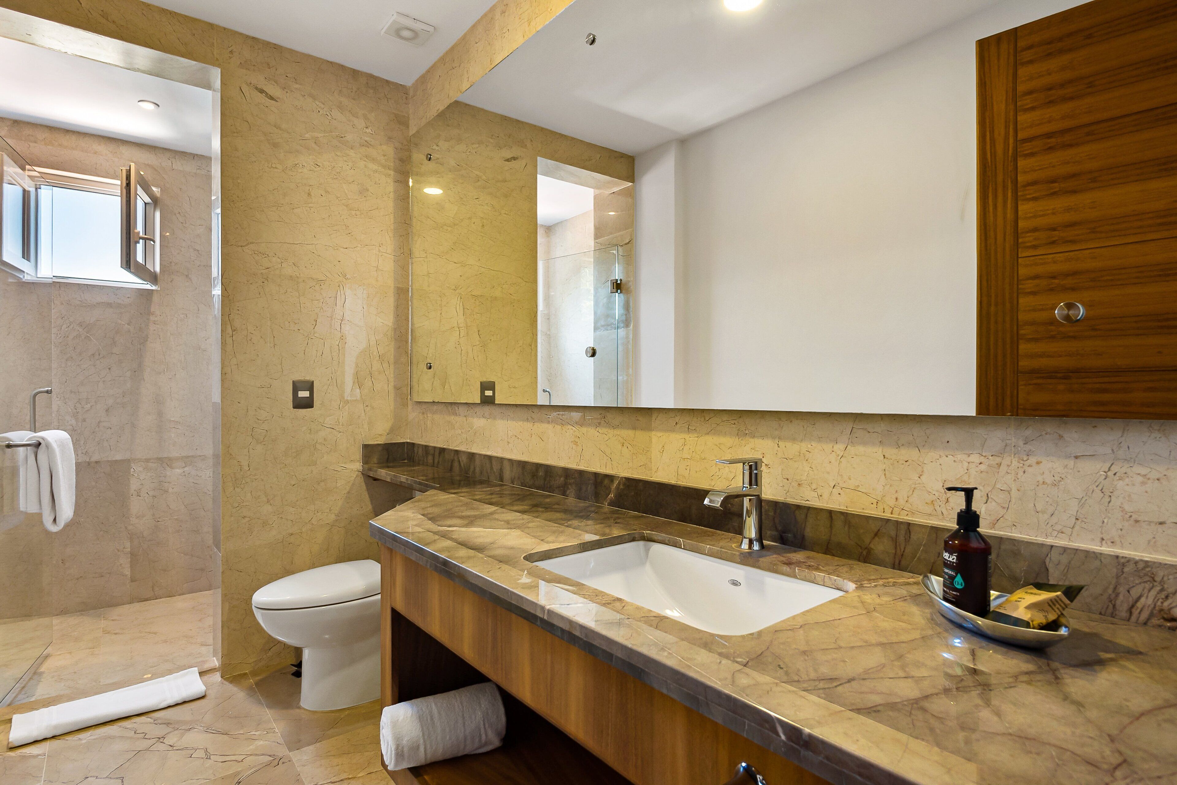 A bathroom with a marble countertop, a sink, a toilet, a shower area, and a wooden cabinet.