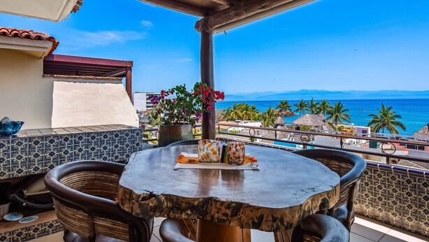 A round table with chairs on a balcony overlooking the sea, with a potted plant and a vase of flowers. - Oceanfront Condo With Pool, Balcony, Amazing Views, Washer/dryer, & Partial AC (Punta de Mita)