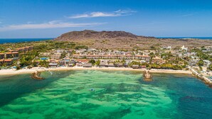 An aerial view of a coastal resort with multiple buildings, clear turquoise waters, and a mountain in the background. - Oceanfront Condo With Pool, Balcony, Amazing Views, Washer/dryer, & Partial AC (Punta de Mita)