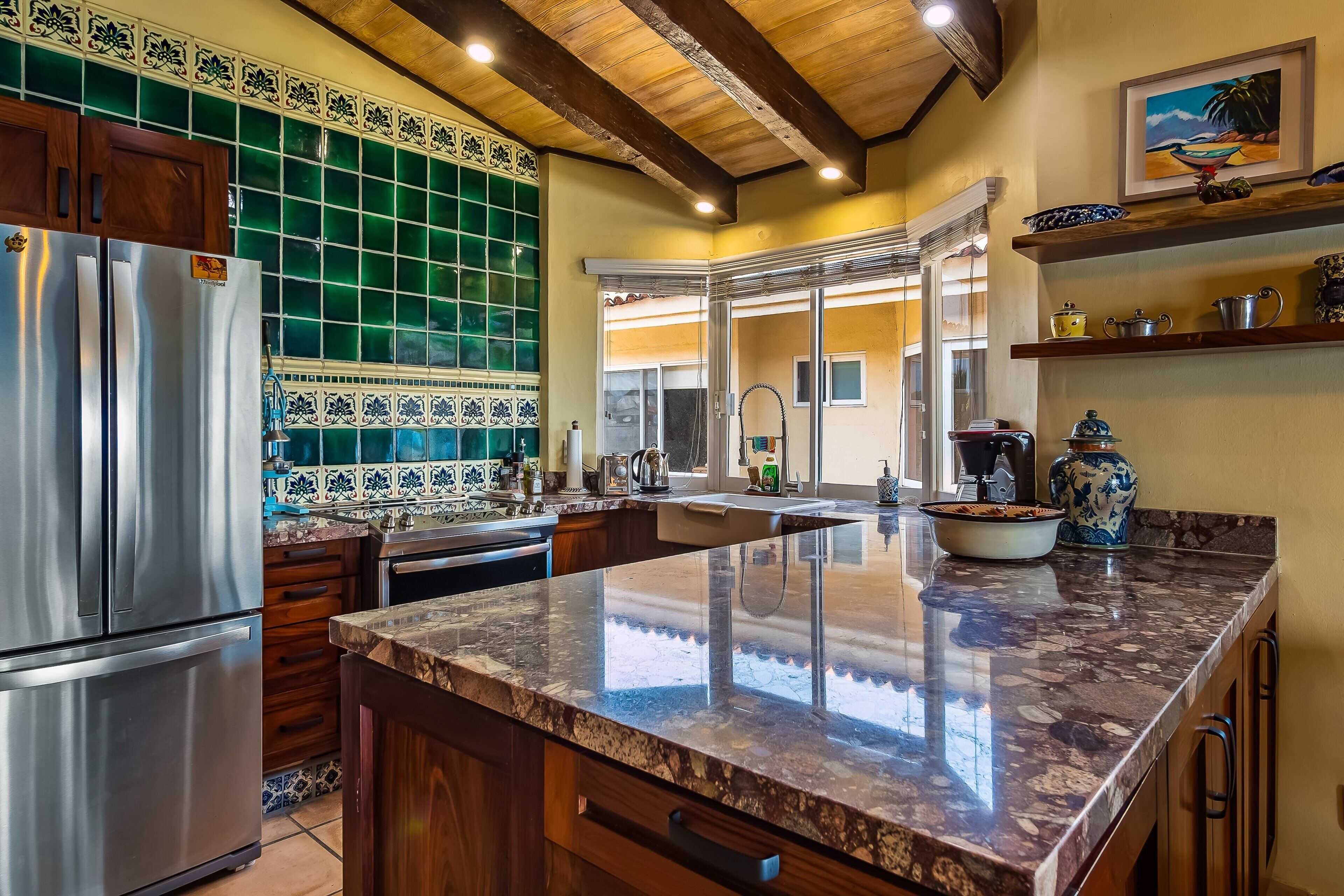 A kitchen with a stainless steel refrigerator, a marble countertop, and a green-tiled backsplash.