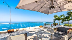 An outdoor seating area with a view of the sea, a large umbrella, and potted plants. - Upscale Coastal Suite With Private Terrace, Ocean Views, Pool & hot tub (Puerto Vallarta)