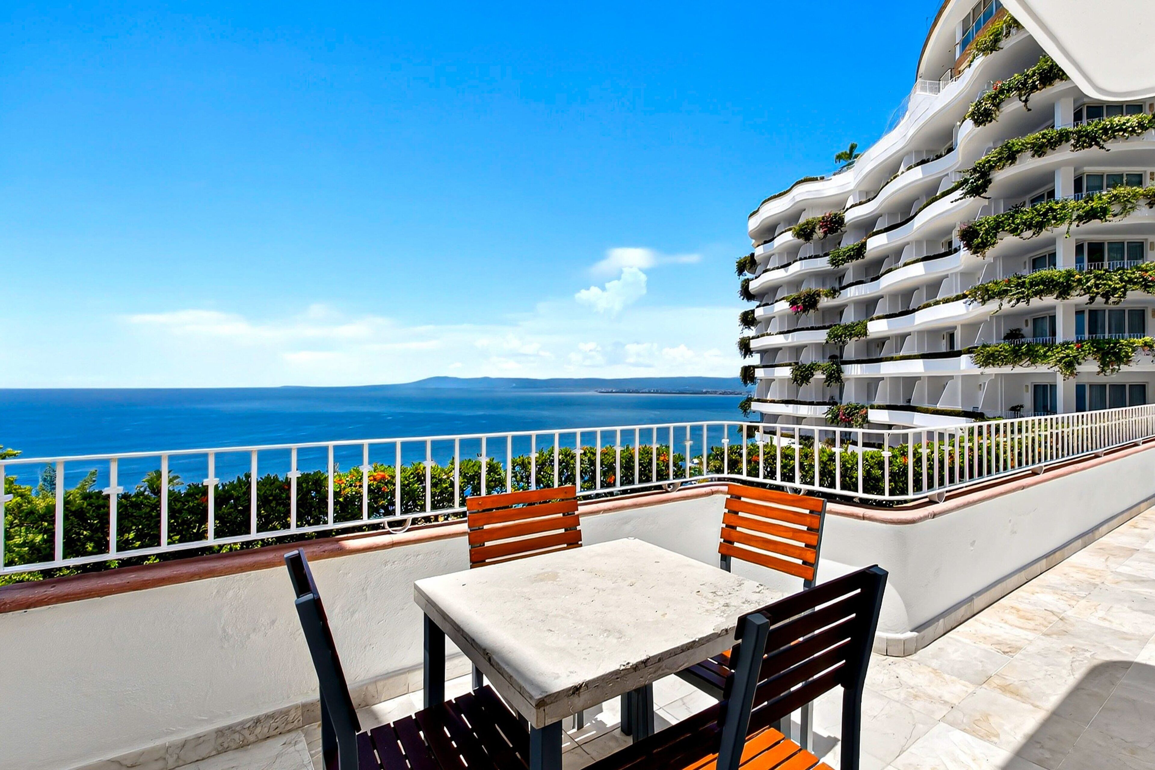 A balcony with a table and chairs, overlooking a sea view.