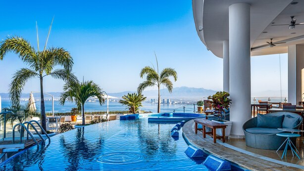 A pool area with palm trees, a view of the city, and a modern interior design. - Upscale Coastal Suite With Private Terrace, Ocean Views, Pool & hot tub (Puerto Vallarta)