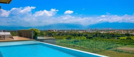 A rooftop infinity pool with a clear view of a cityscape and mountains.