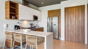 Een moderne keuken met een centraal eiland, barstoelen, een ingebouwde magnetron, een roestvrijstalen koelkast en houten kastjes.
