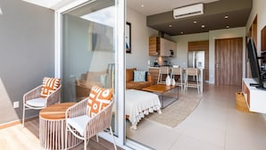 Een moderne zithoek met een glazen deur naar een keuken, een eetgedeelte met tafel en stoelen, en een bank met decoratieve kussens.
