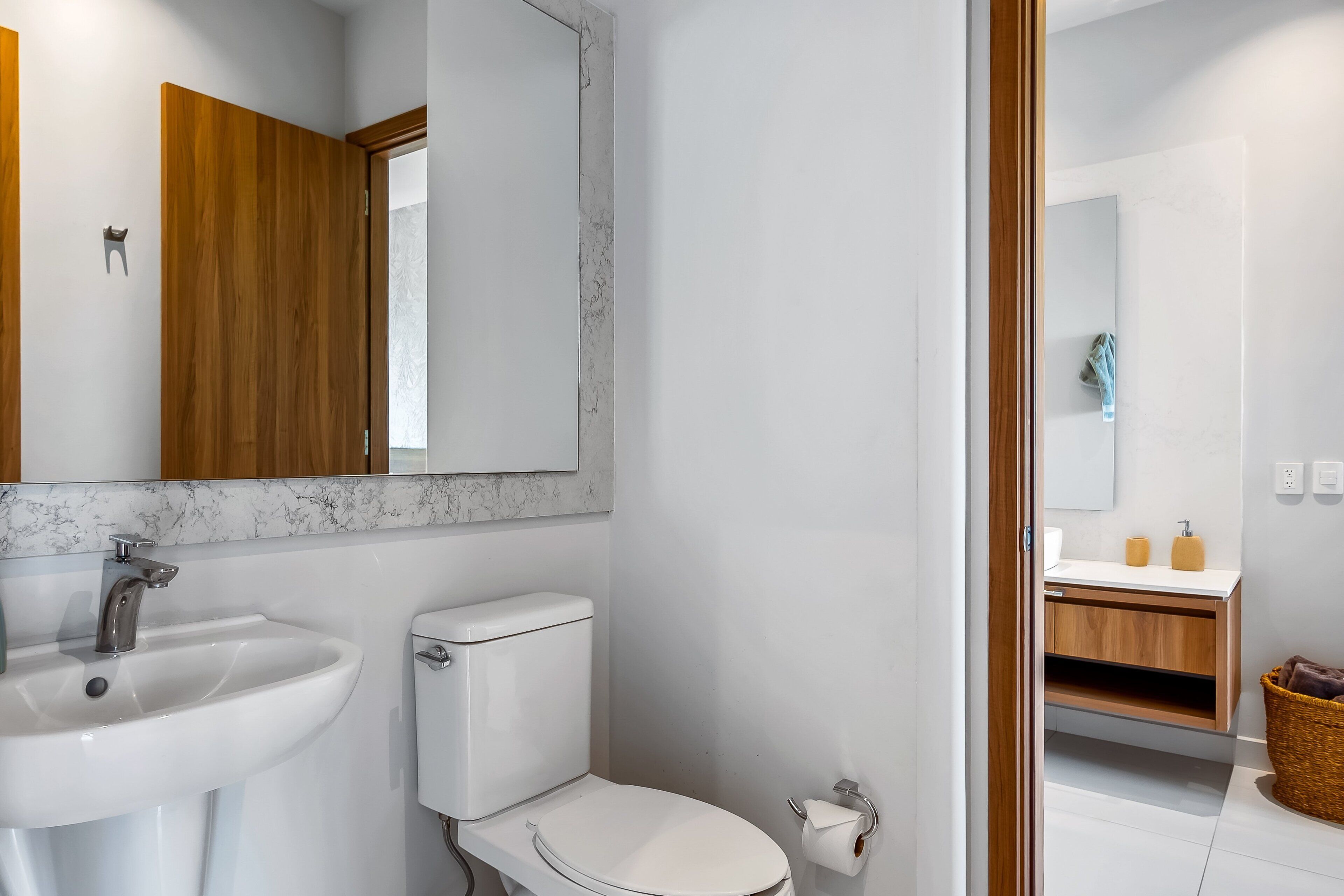 A bathroom with a white sink, toilet, and mirror, wooden cabinets, and a marble backsplash.