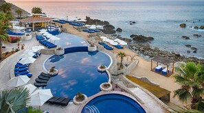 A resort pool with blue lounge chairs and umbrellas, surrounded by a rocky coastline. - Charming 2-bedroom villa with AC in Cabo San Lucas (Cabo San Lucas,)