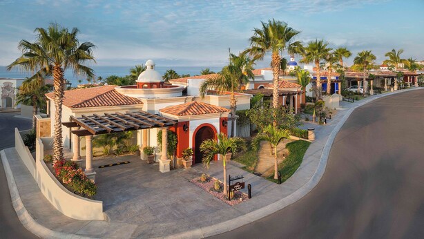 Een hotel in mediterrane stijl, met een centrale binnenplaats, palmbomen en uitzicht op zee.